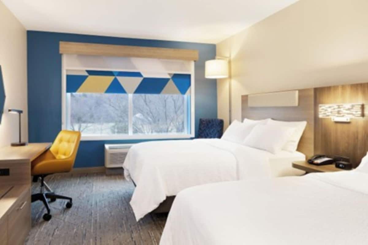 Ein Hotelzimmer mit zwei Betten, einem Schreibtisch, einem Stuhl, einem Fenster mit Blick und einer Wandlampe.