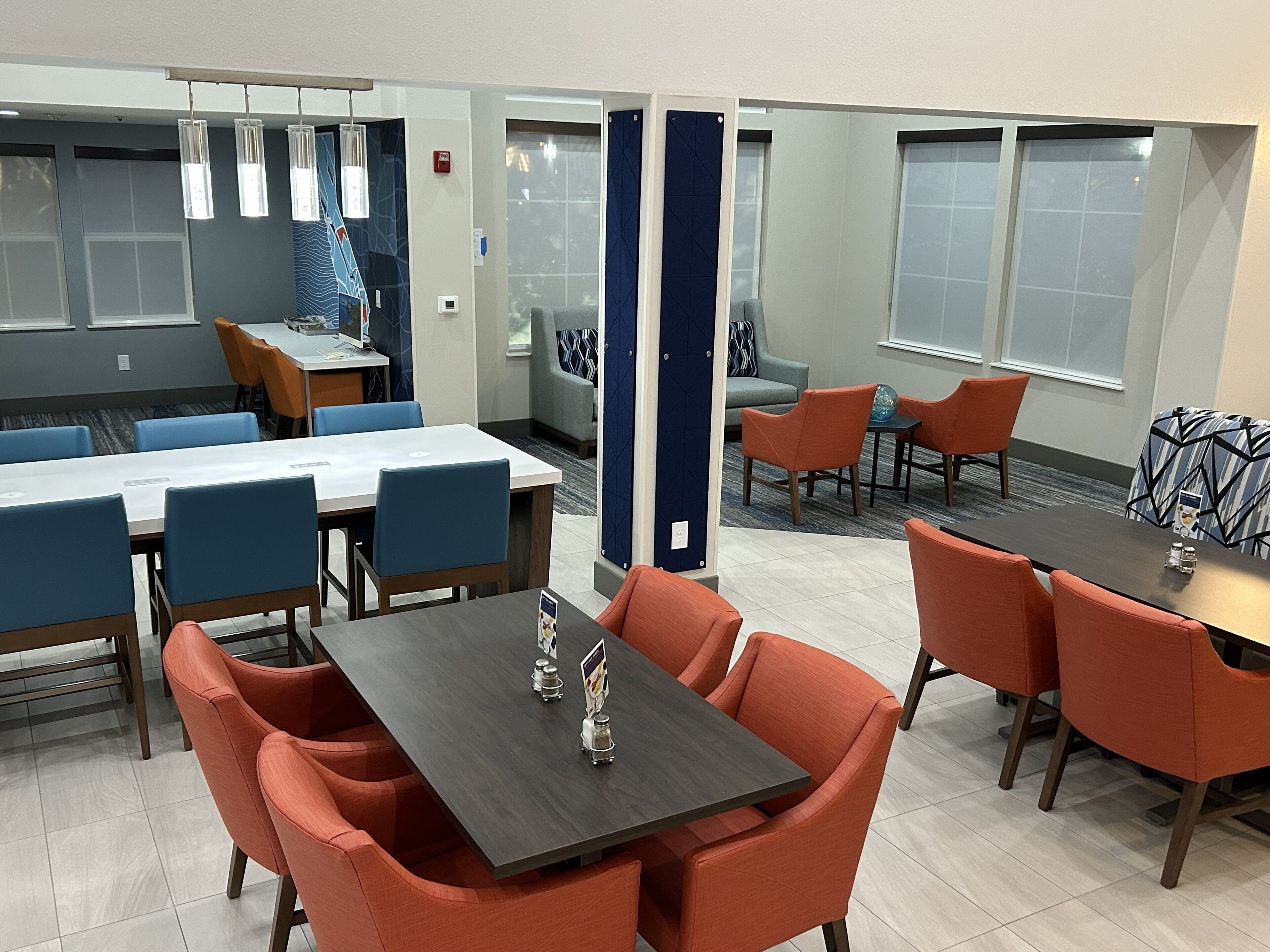 A modern hotel lobby with a dining area, seating arrangements, and a reception desk.