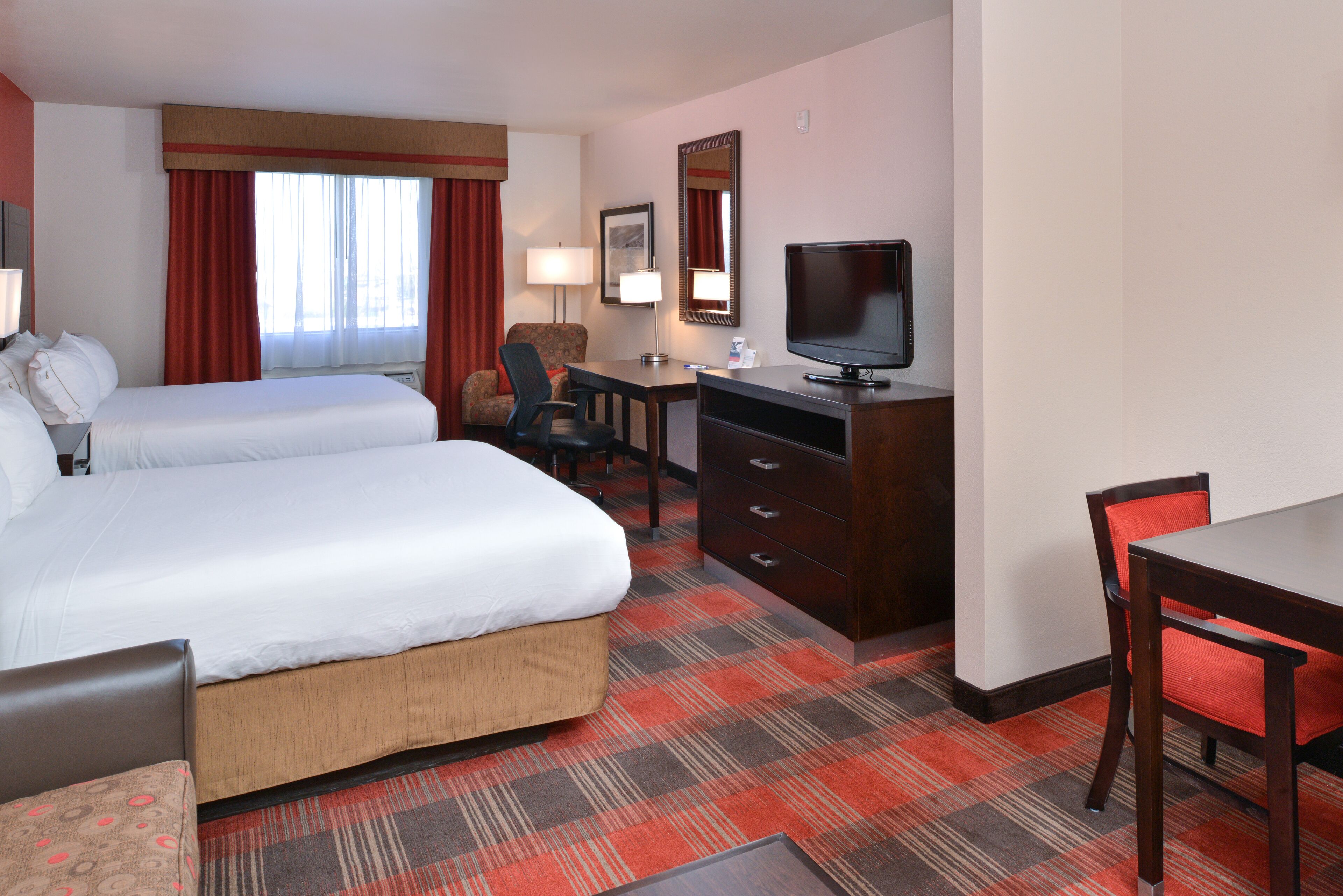 A hotel room with two beds, a desk with a chair, a television, and a dresser.