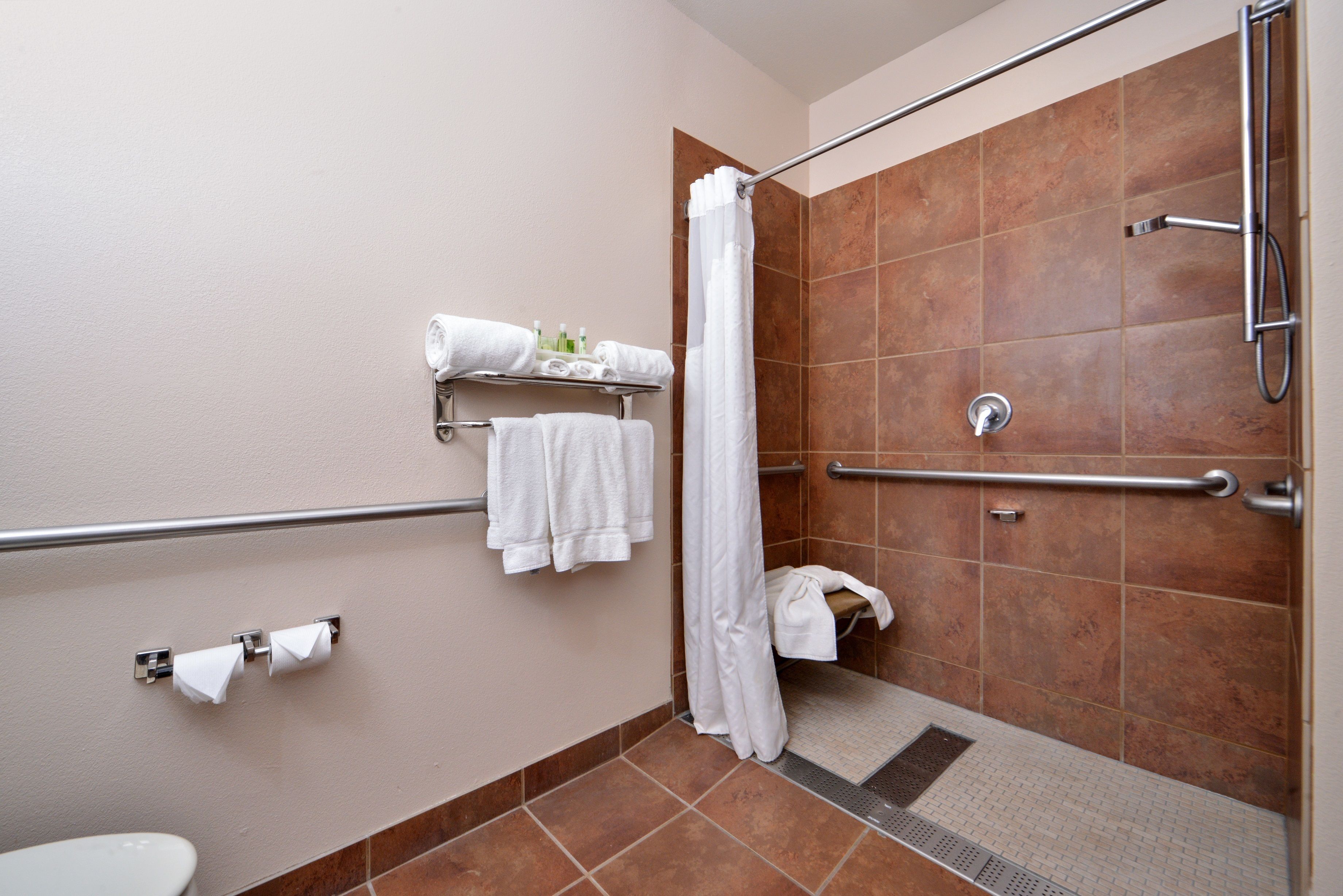 A bathroom with a shower, a toilet, and a towel rack with towels.