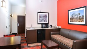 A compact hotel room with a kitchenette, a sofa, a dining table, and a red accent wall. - Holiday Inn Express Hotel & Suites Kingman by IHG (Kingman)