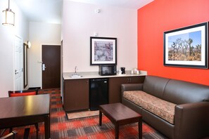 A compact hotel room with a kitchenette, a sofa, a dining table, and a red accent wall. - Holiday Inn Express Hotel & Suites Kingman by IHG (Kingman)