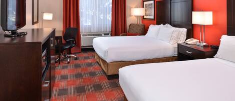 A hotel room with two beds, a desk with a television, a chair, a desk lamp, and a bedside table with a lamp.