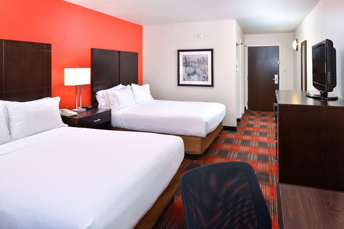 A hotel room with two beds, a desk with a lamp, a television, and a framed picture on the wall.