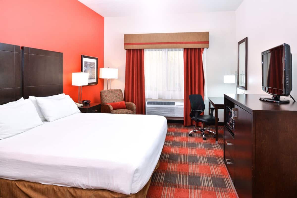 A hotel room with a large bed, a desk with a computer, a chair, a lamp, and a television.
