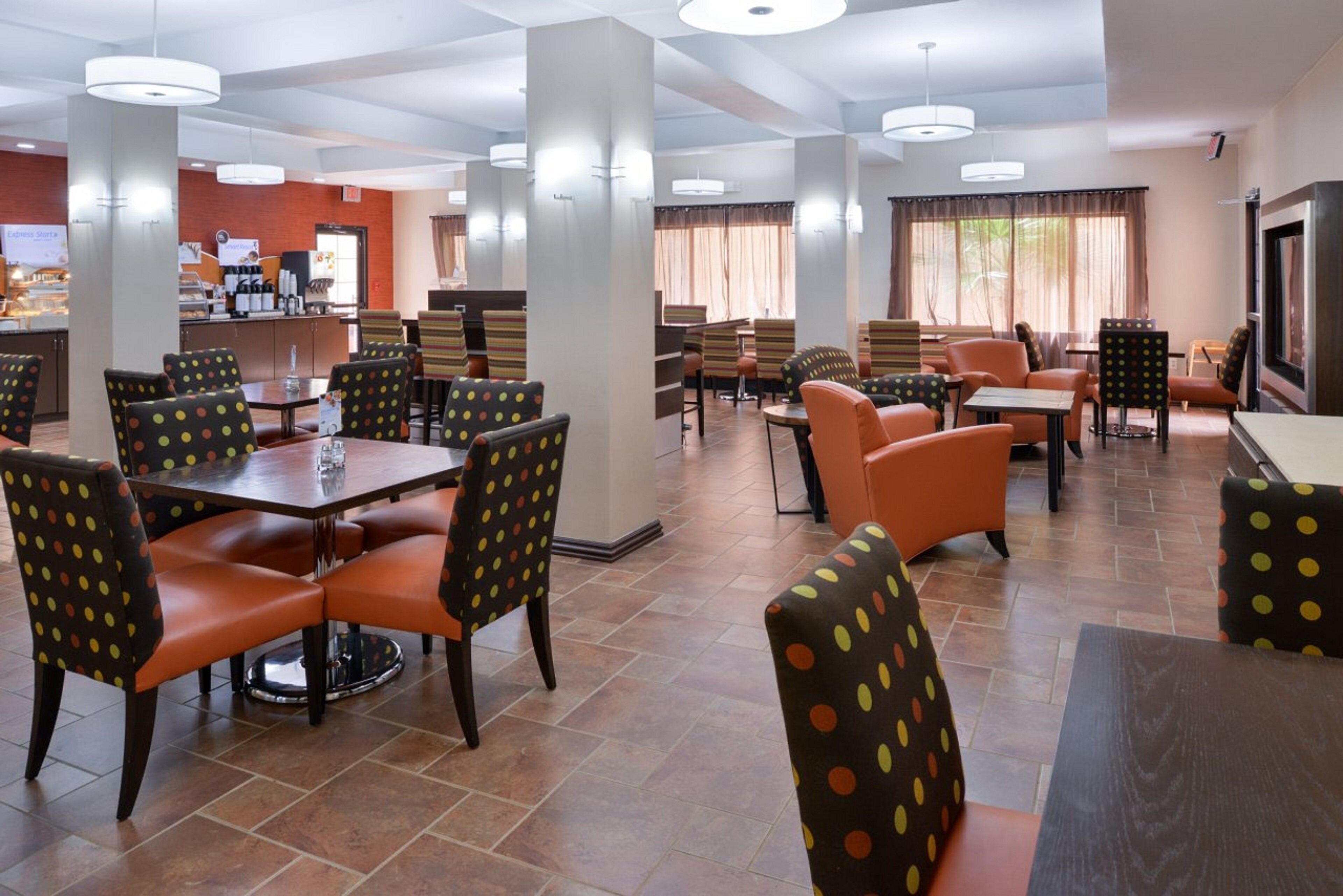 A hotel dining area with multiple tables and chairs, a buffet counter, and a large window with curtains.