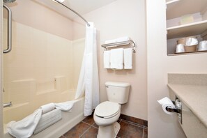 A bathroom with a bathtub, toilet, and a shelf with toiletries. - Holiday Inn Express Hotel & Suites Kingman by IHG (Kingman)