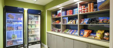 Two refrigerated display cases with various food items, a shelf stocked with snacks, and a counter with packaged goods.