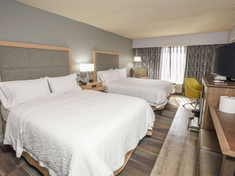 A hotel room with two beds, a desk with a television, and a chair.