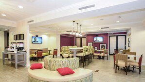 A modern hotel lobby with a circular seating area, multiple dining tables, and televisions on the walls. - Hampton Inn Jacksonville East Regency Square (Jacksonville)