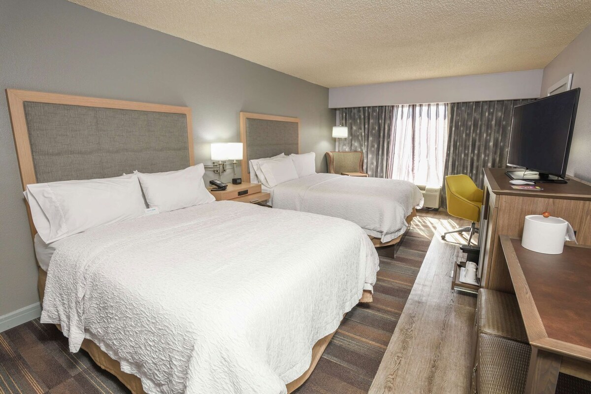 A hotel room with two beds, a desk, a television, and a chair.