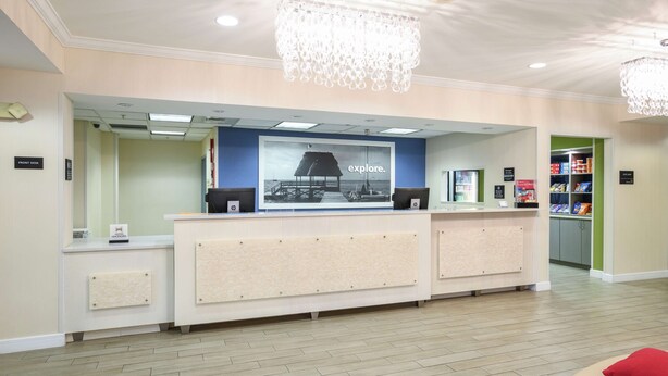 A reception area with a counter, a large framed poster, and a chandelier. - Hampton Inn Jacksonville East Regency Square (Jacksonville)