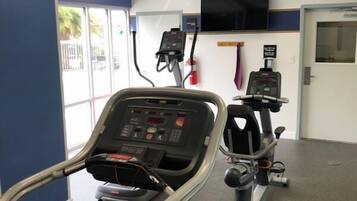 A fitness room with treadmills and a stationary bike, a television on the wall, and a fire extinguisher.