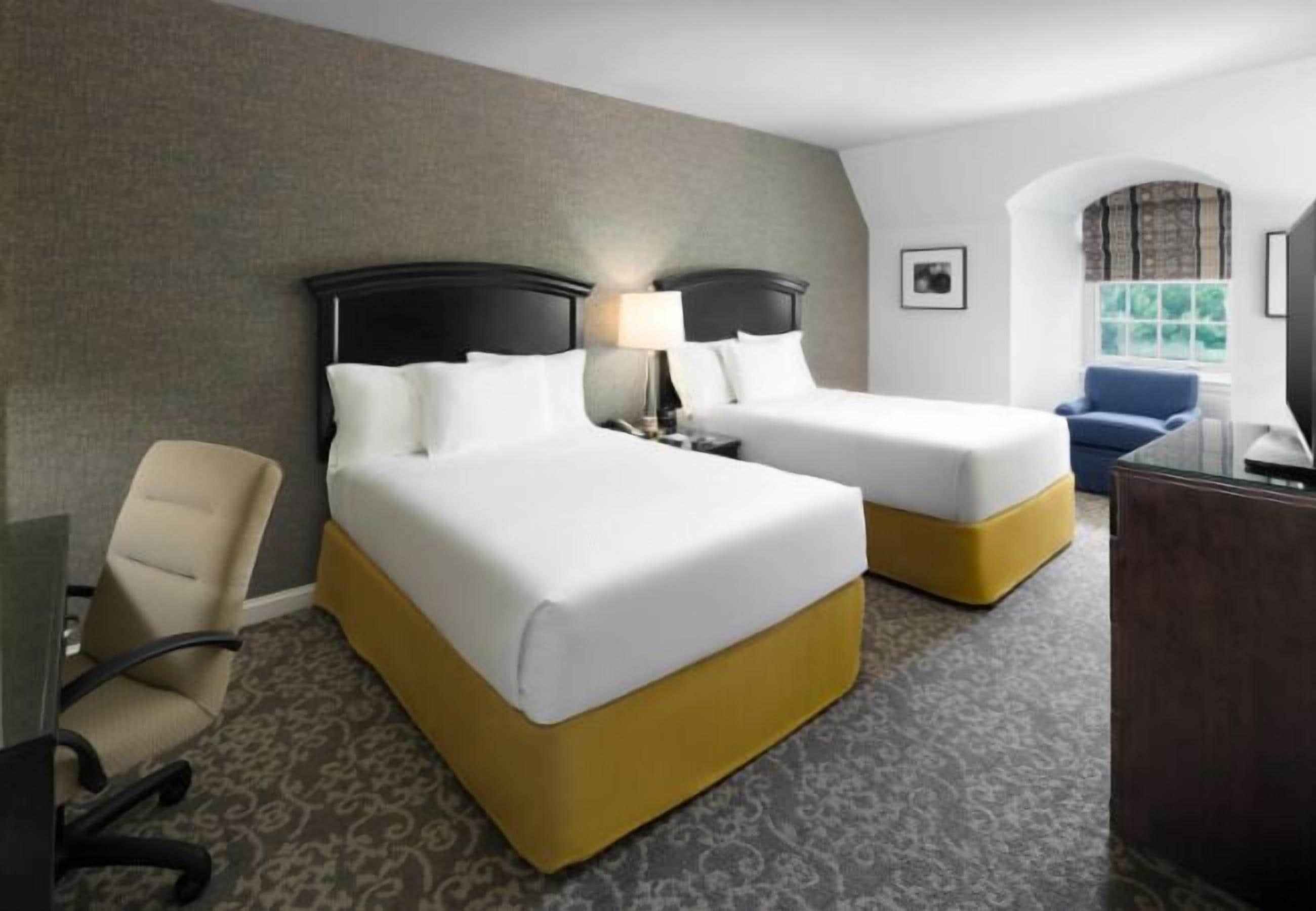Une chambre d’hôtel avec deux lits, un bureau, une chaise et une fenêtre donnant sur un paysage agréable.