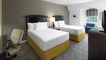 A hotel room with two beds, a desk, a chair, and a television.