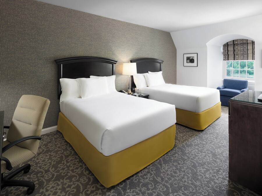 A hotel room with two beds, a desk, a chair, and a television.