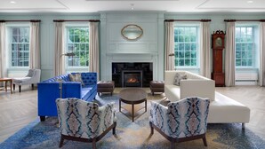 Un salon spacieux avec une cheminée, des fauteuils à motifs bleus et blancs, un canapé bleu et un canapé blanc.