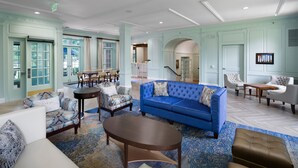 Un hall d’entrée spacieux, avec un canapé bleu, des fauteuils à motifs et une table basse.