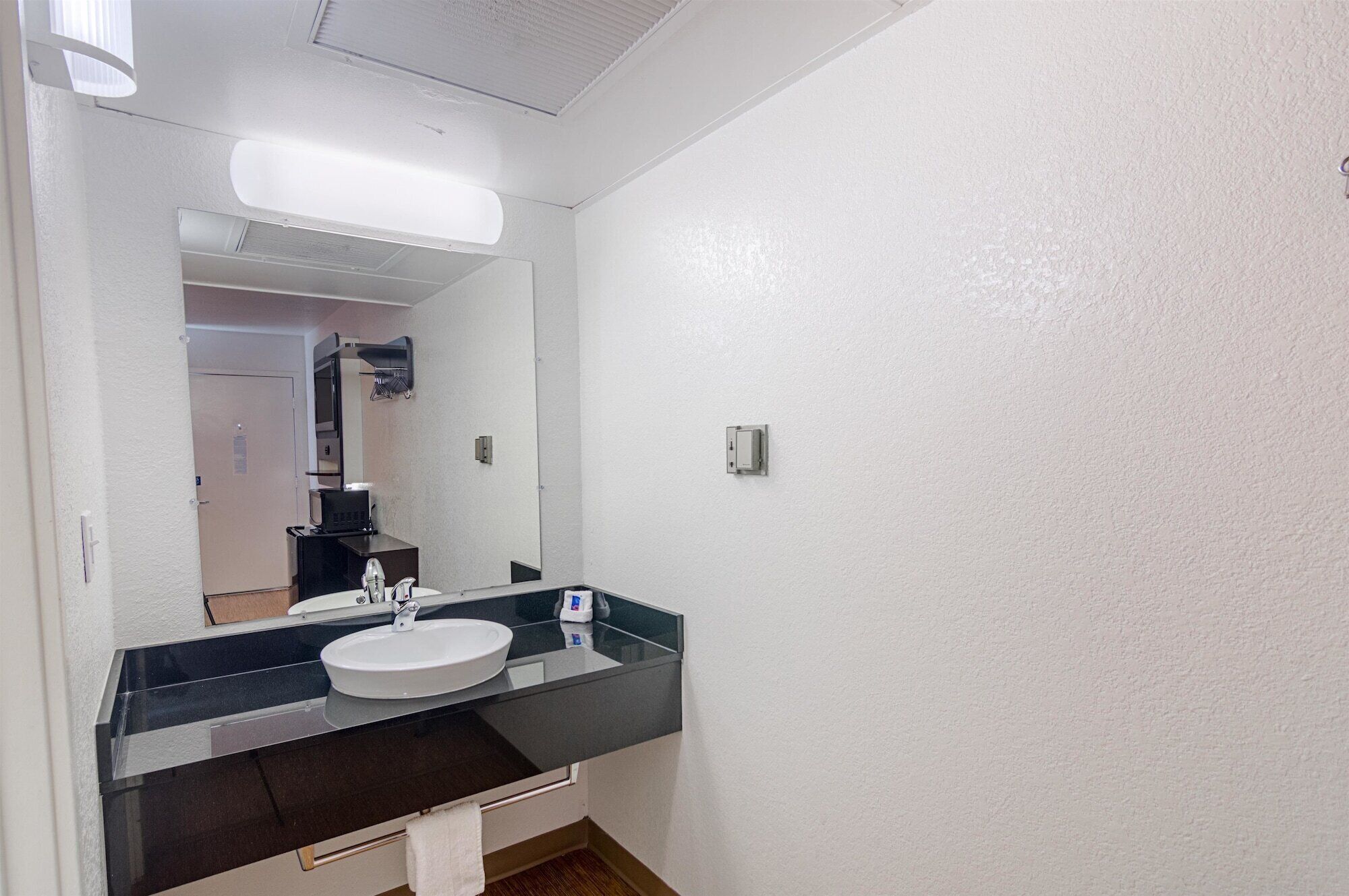 A bathroom with a white sink, a large mirror, and a black countertop.