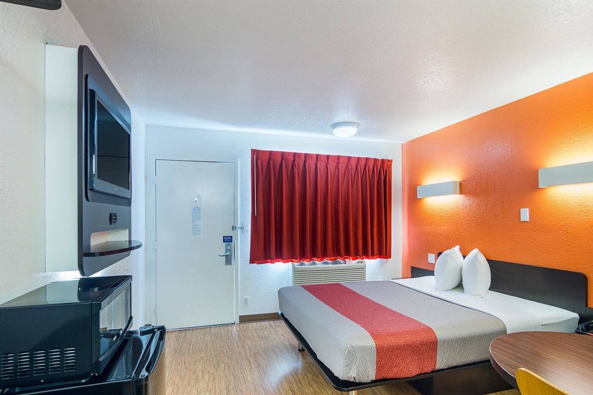 A hotel room with a bed, a desk, a TV, and a red curtain.
