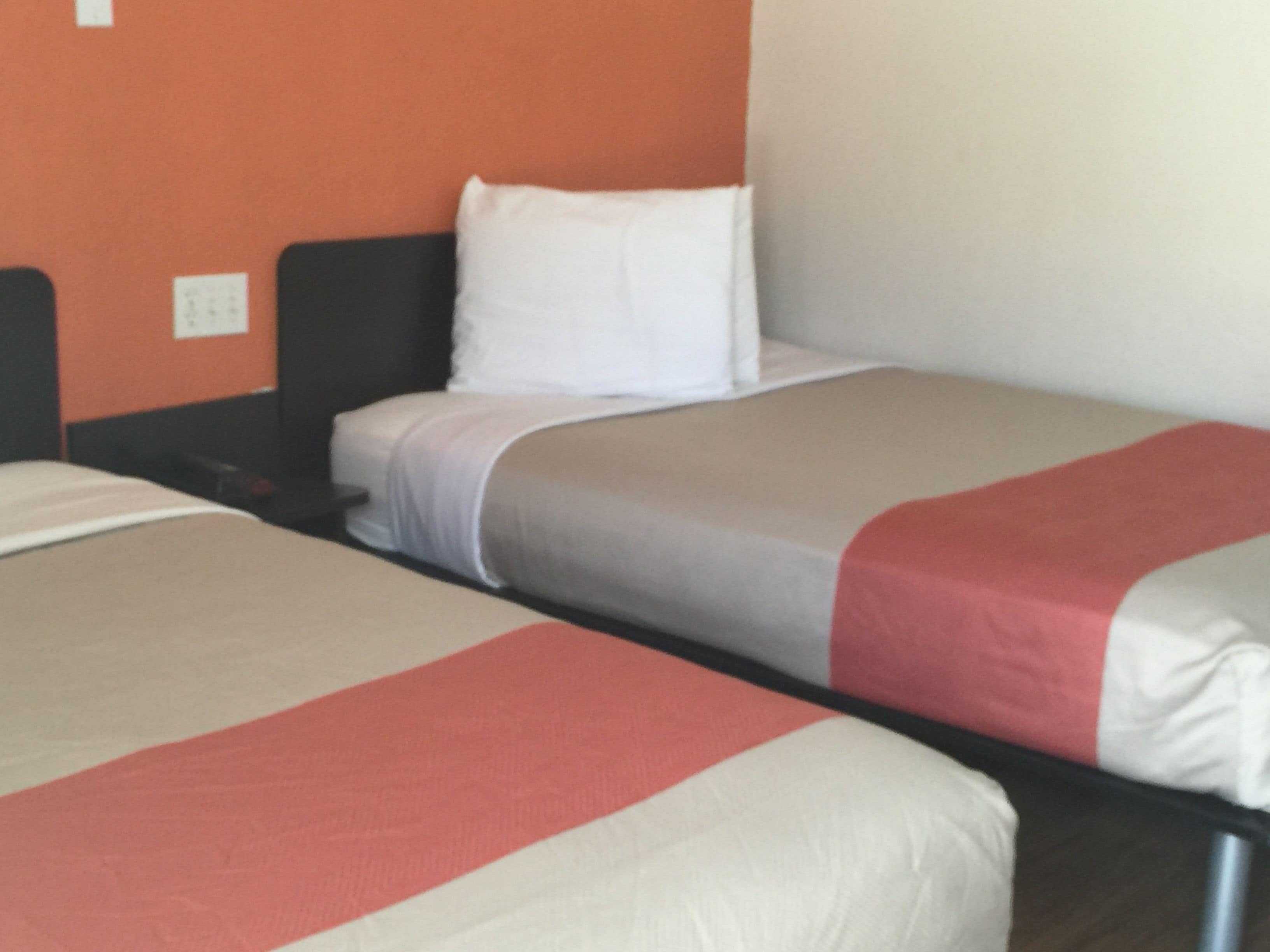 A hotel room with two single beds, each with a white pillow and a red and beige bedspread.