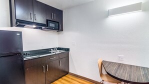 Une cuisine compacte avec des meubles de couleur sombre, un four à micro-ondes, un évier et une petite table avec une chaise.