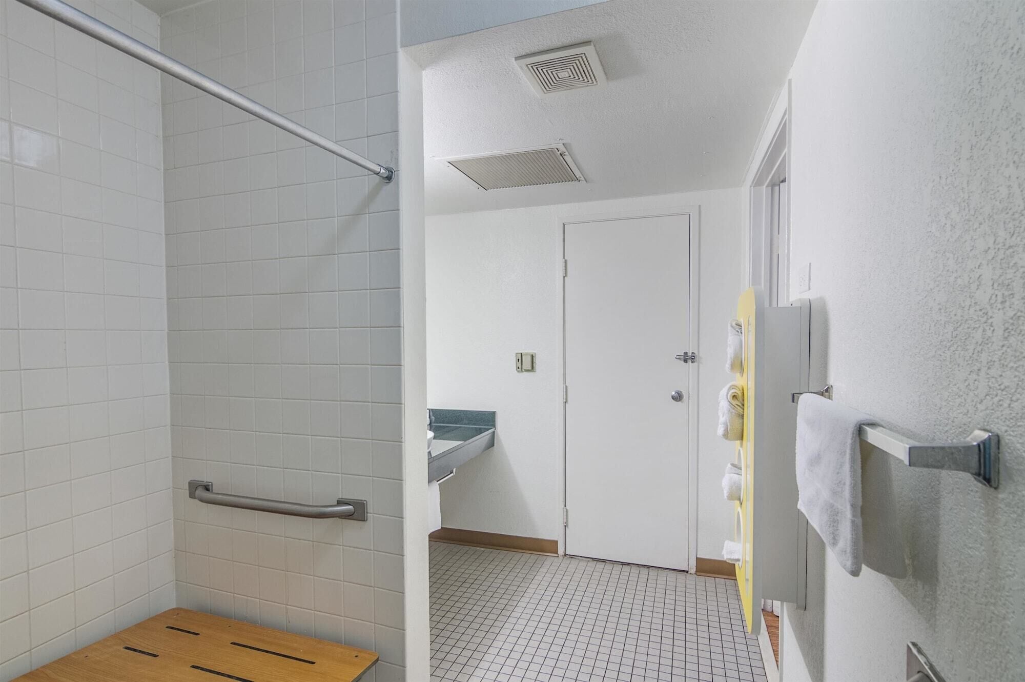A bathroom with white tiled walls, a wooden bench, a handrail, a sink, and a door.