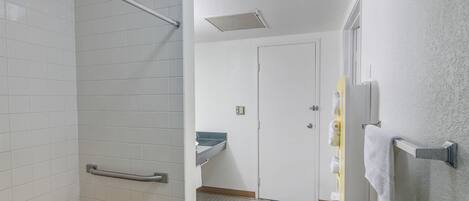 A bathroom with white tiled walls, a wooden bench, a handrail, a sink, and a door.