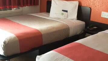 A hotel room with two beds, each with a white and orange bedspread, a white pillow, and a small bedside table with a phone and a book.