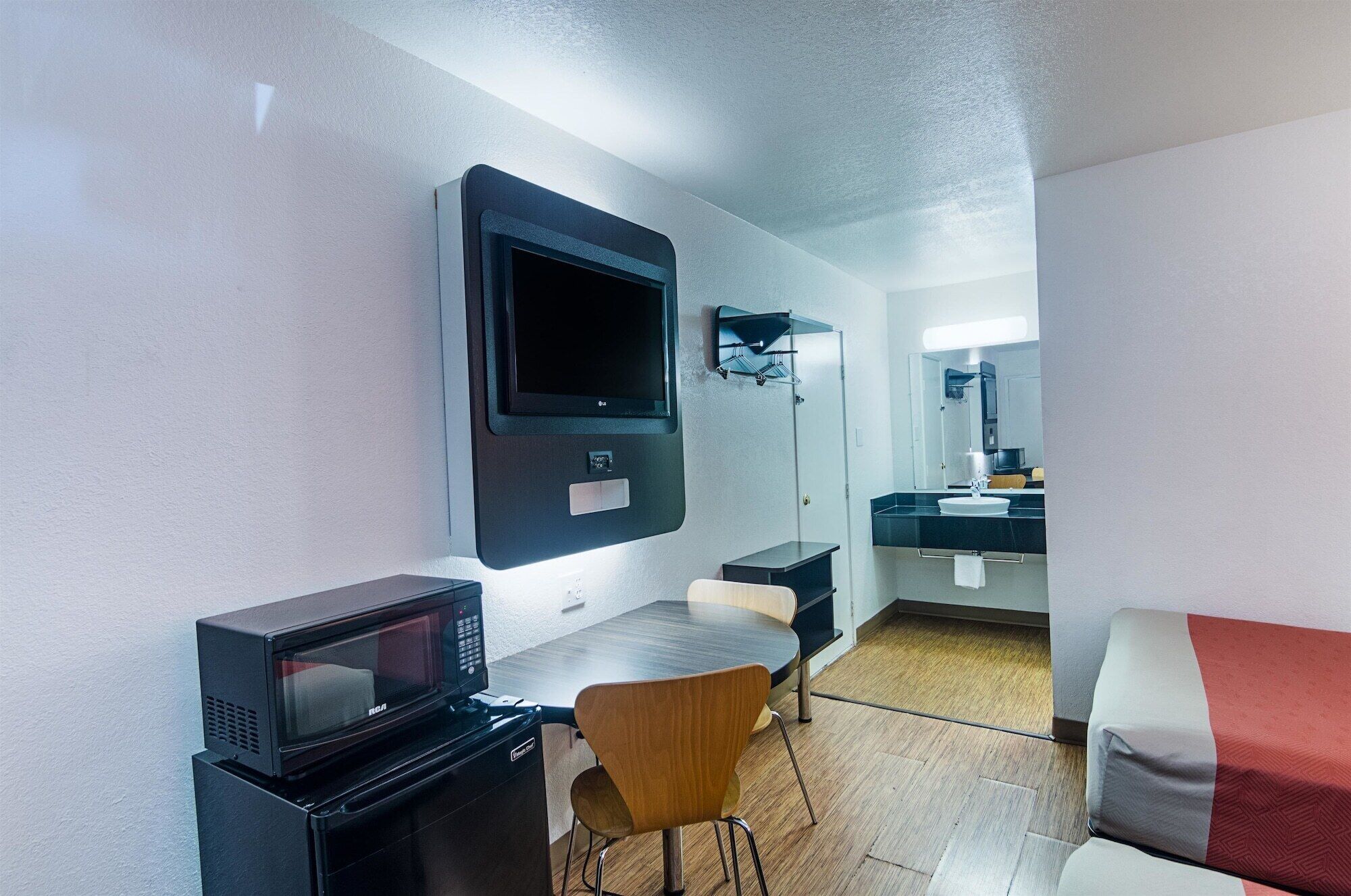 Ett kompakt hotellrum med ett litet pentry, en platt-TV som är monterad på väggen, en mikrovågsugn, ett litet bord och en stol.
