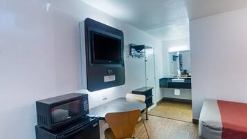 Ett kompakt hotellrum med ett litet pentry, en platt-TV som är monterad på väggen, en mikrovågsugn, ett litet bord och en stol.