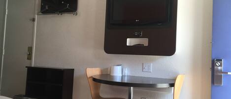 A hotel room with a bed, a desk, two chairs, a television mounted on the wall, and a coat rack.