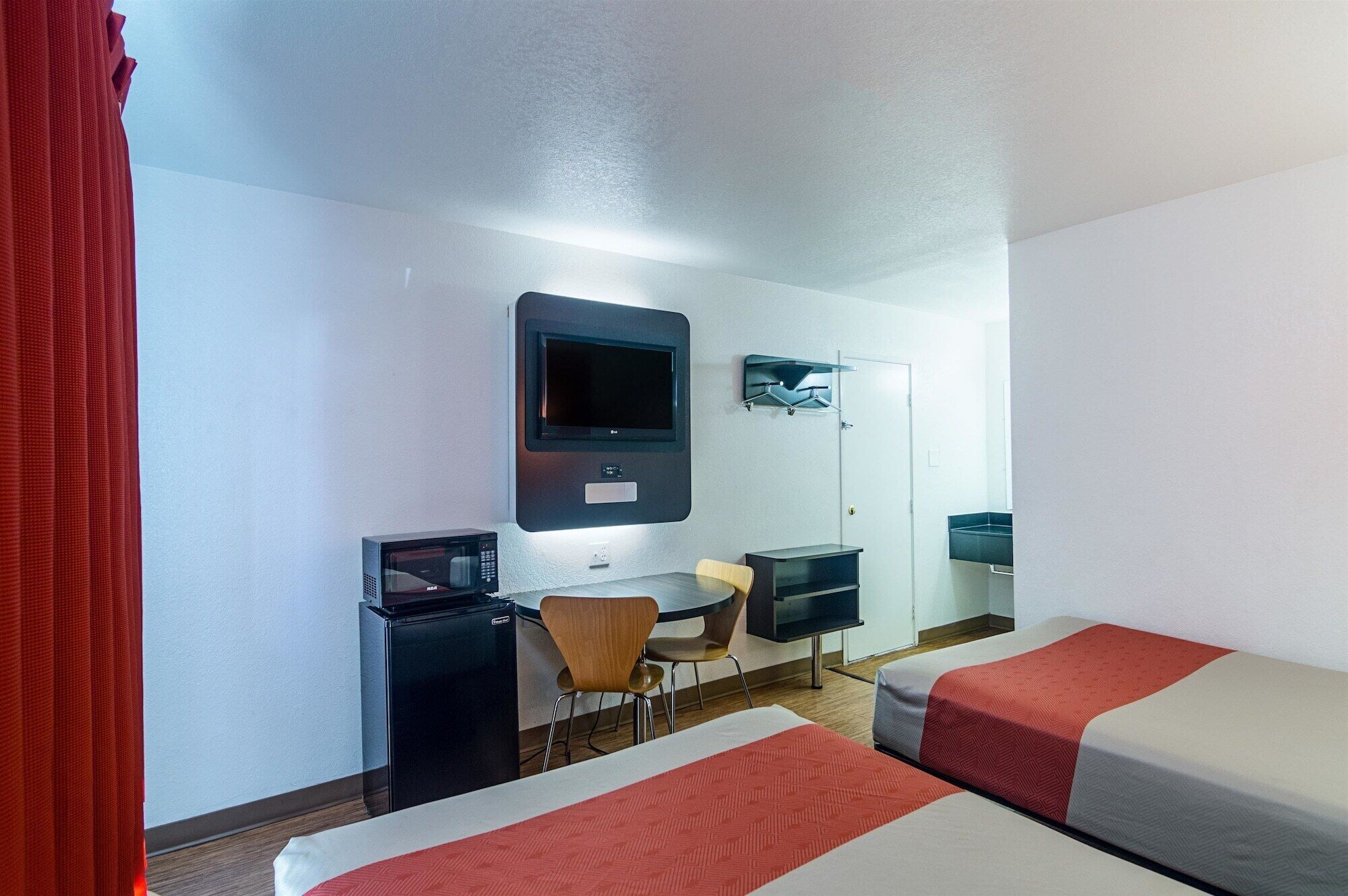 Habitación de hotel con dos camas, un escritorio con microondas, una silla, un televisor montado en la pared y un espejo.