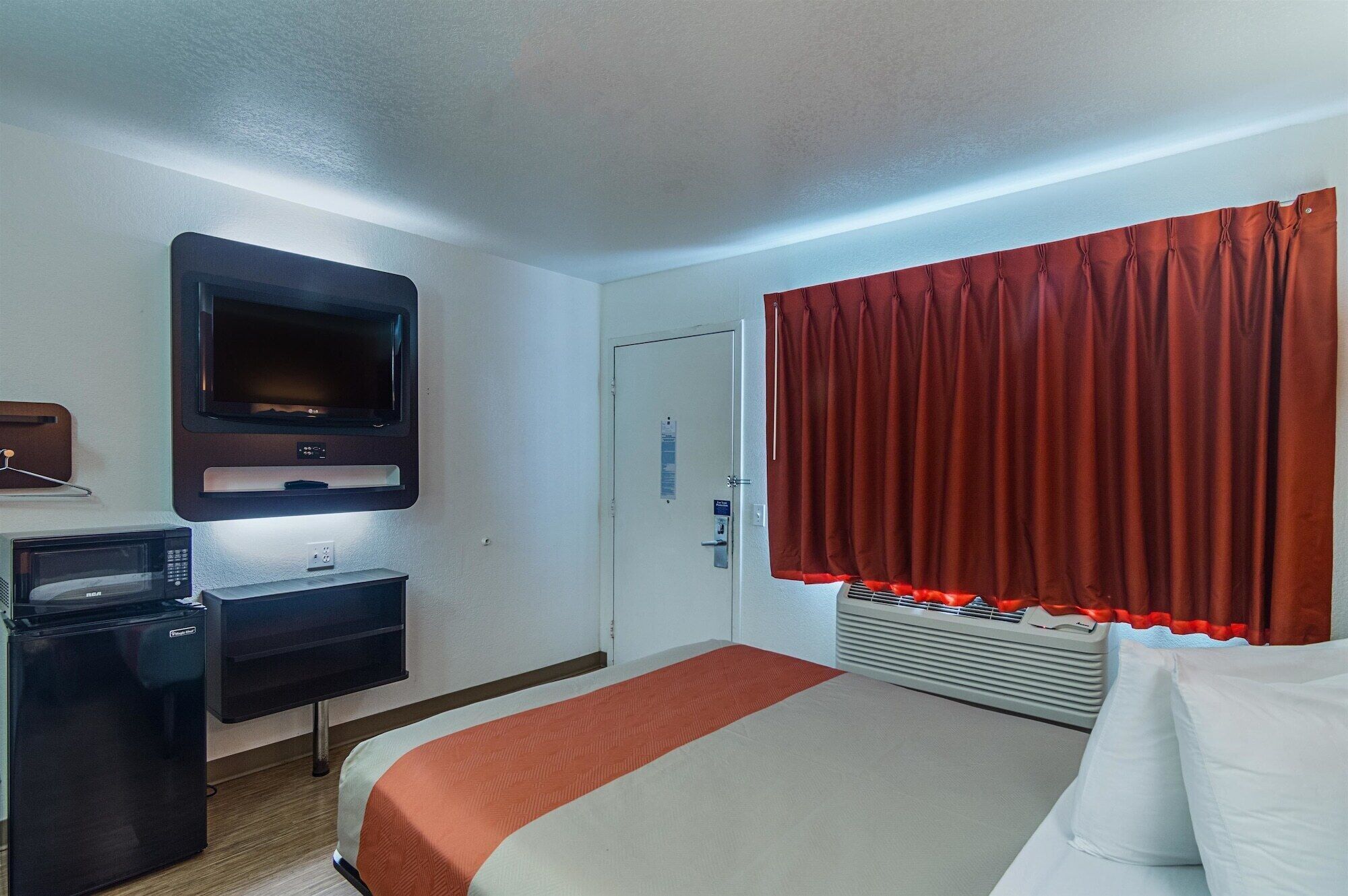 A hotel room with a bed, a TV mounted on the wall, a microwave, and a mini-fridge.