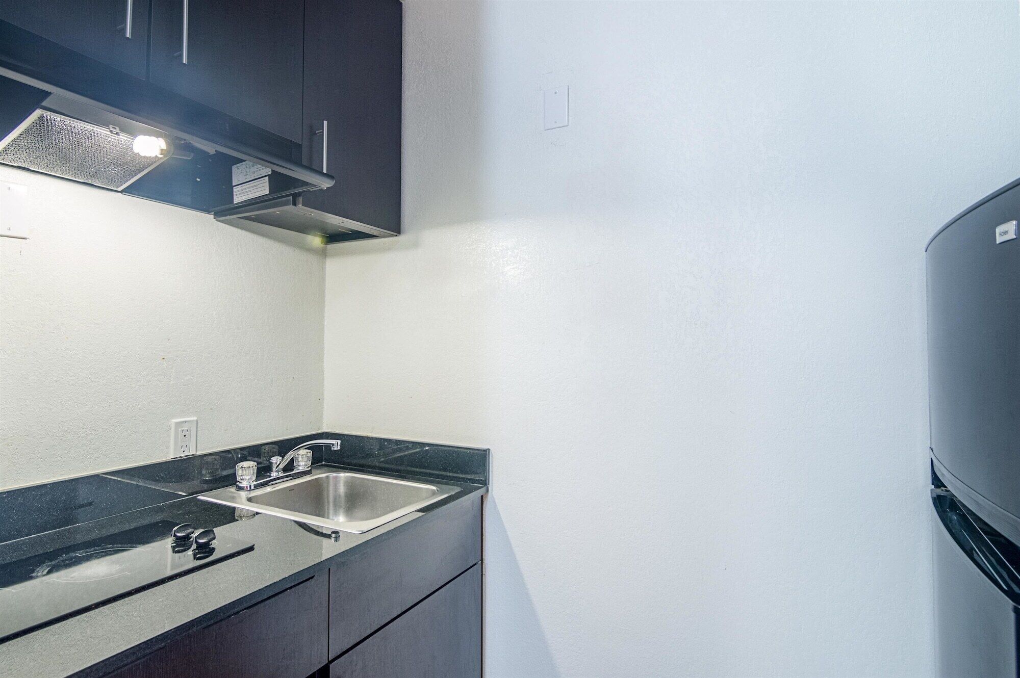 A compact kitchen with dark cabinets, a stainless steel sink, and a black countertop.