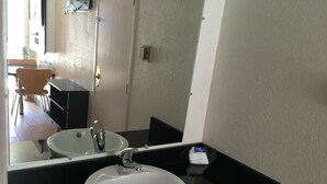 Une salle de bain avec un lavabo blanc, un plan de toilette noir et un miroir qui reflète une porte et une chaise.