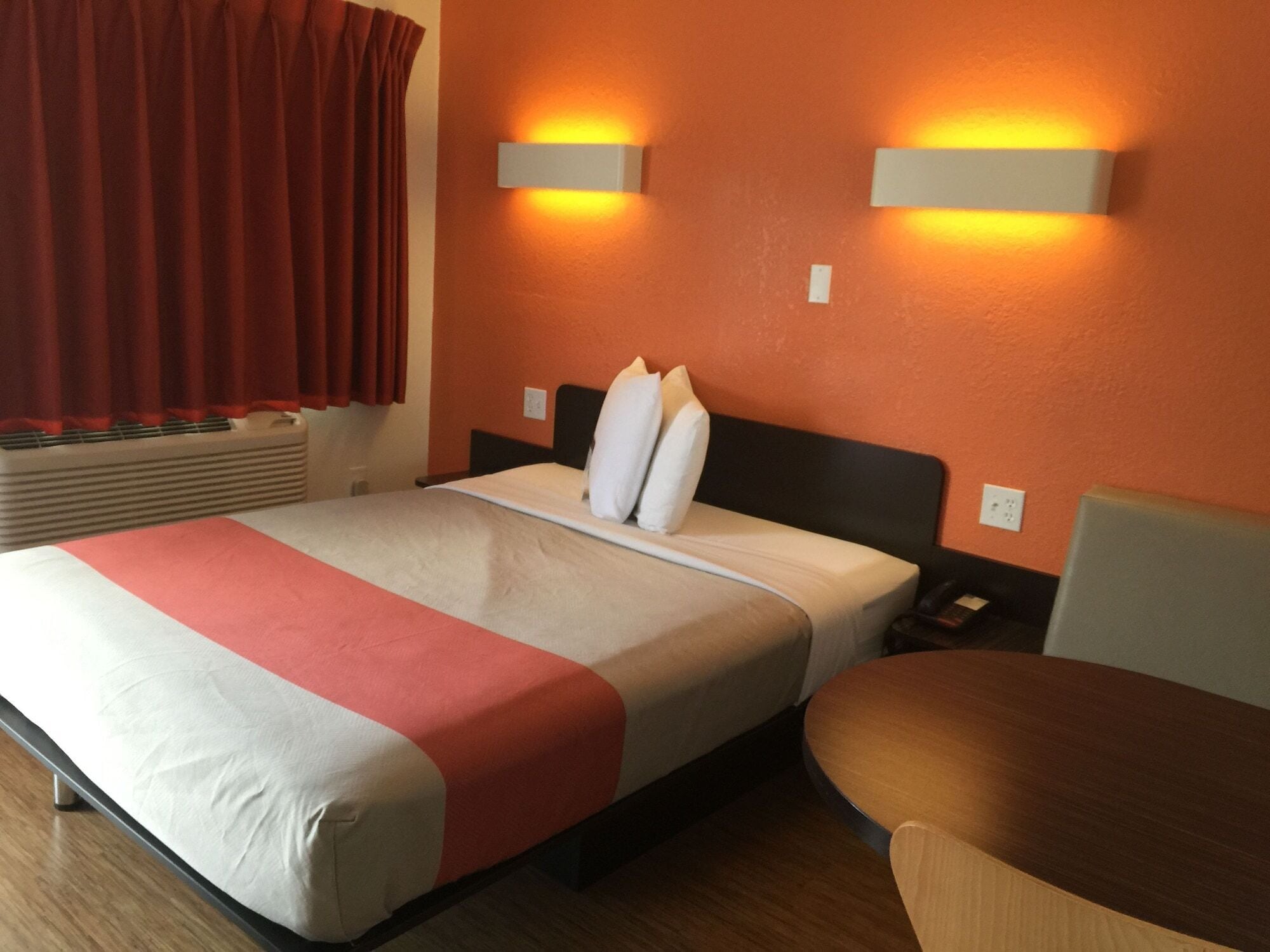 Una habitación de hotel con cama, mesitas de noche, una mesa y una lámpara fijada a la pared.