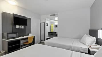 A hotel room with a bed, a desk with a computer, a microwave, a chair, and a bathroom with a mirror and sink.