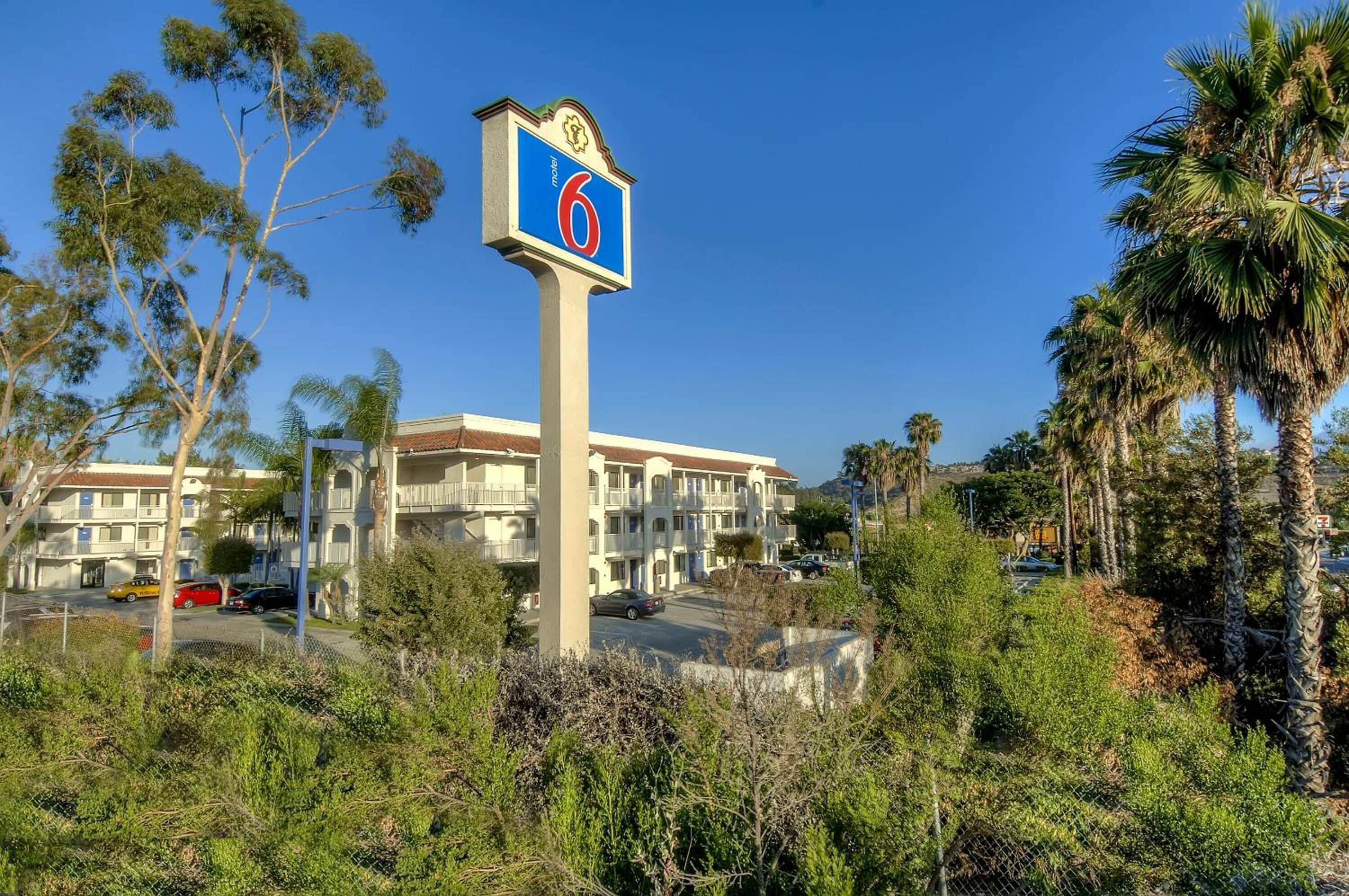 A hotel sign with the number 6, surrounded by greenery and a building with balconies.