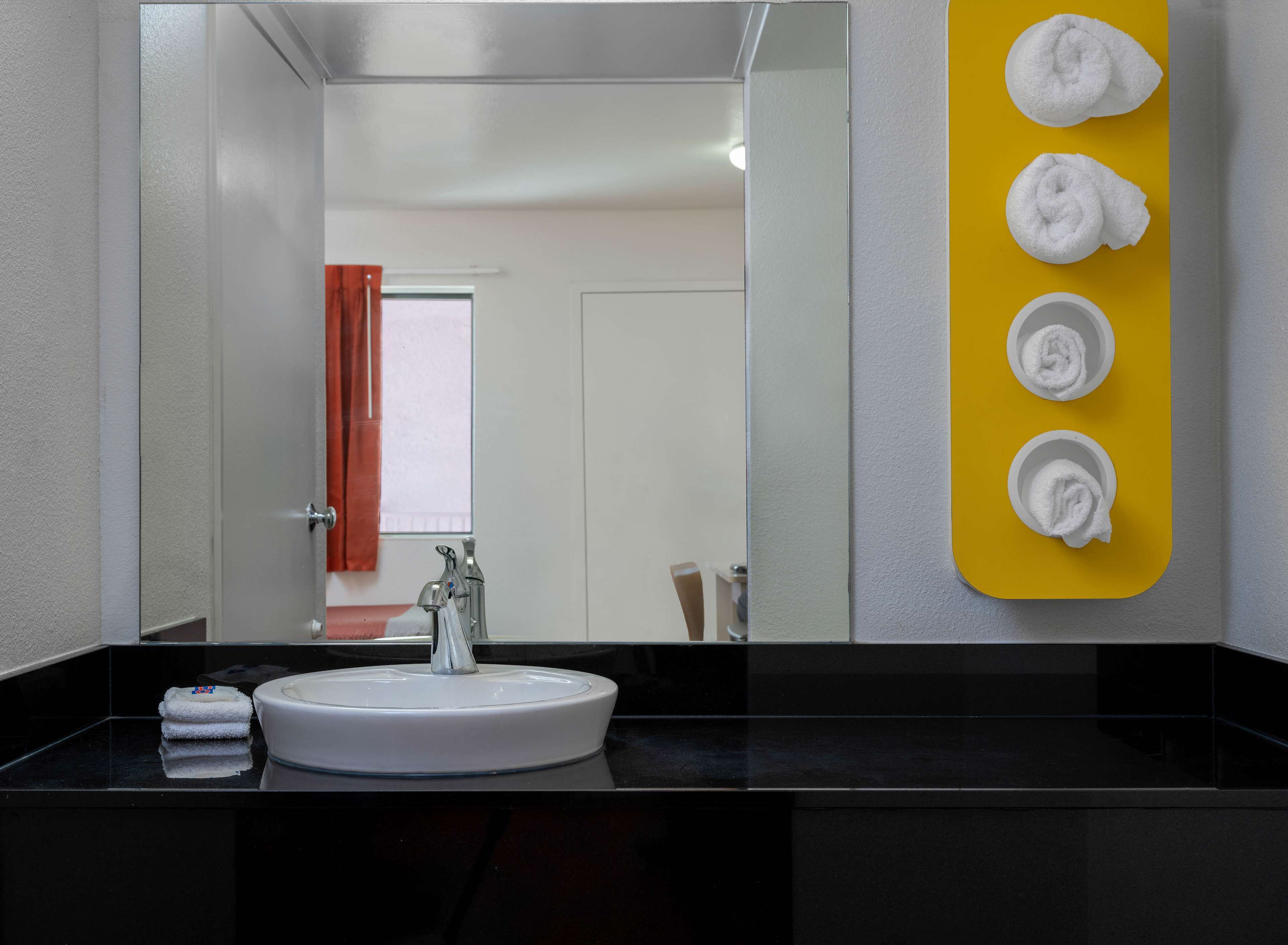 A modern bathroom with a round sink, a mirror, and a yellow towel rack with three towels.