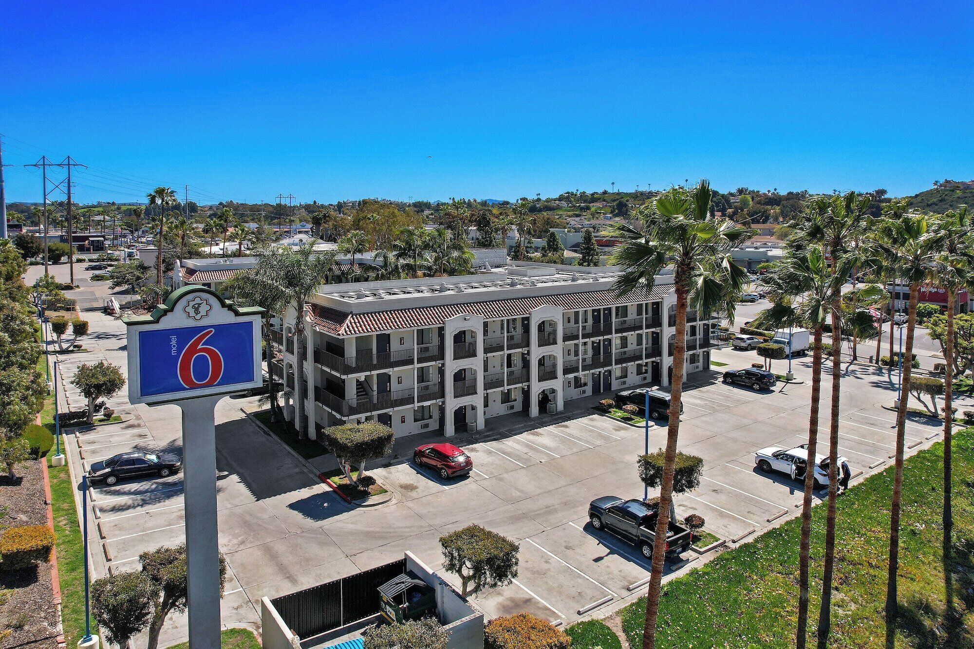 Un motel à plusieurs étages avec un parking, entouré de palmiers et surplombé d’un ciel bleu azur.