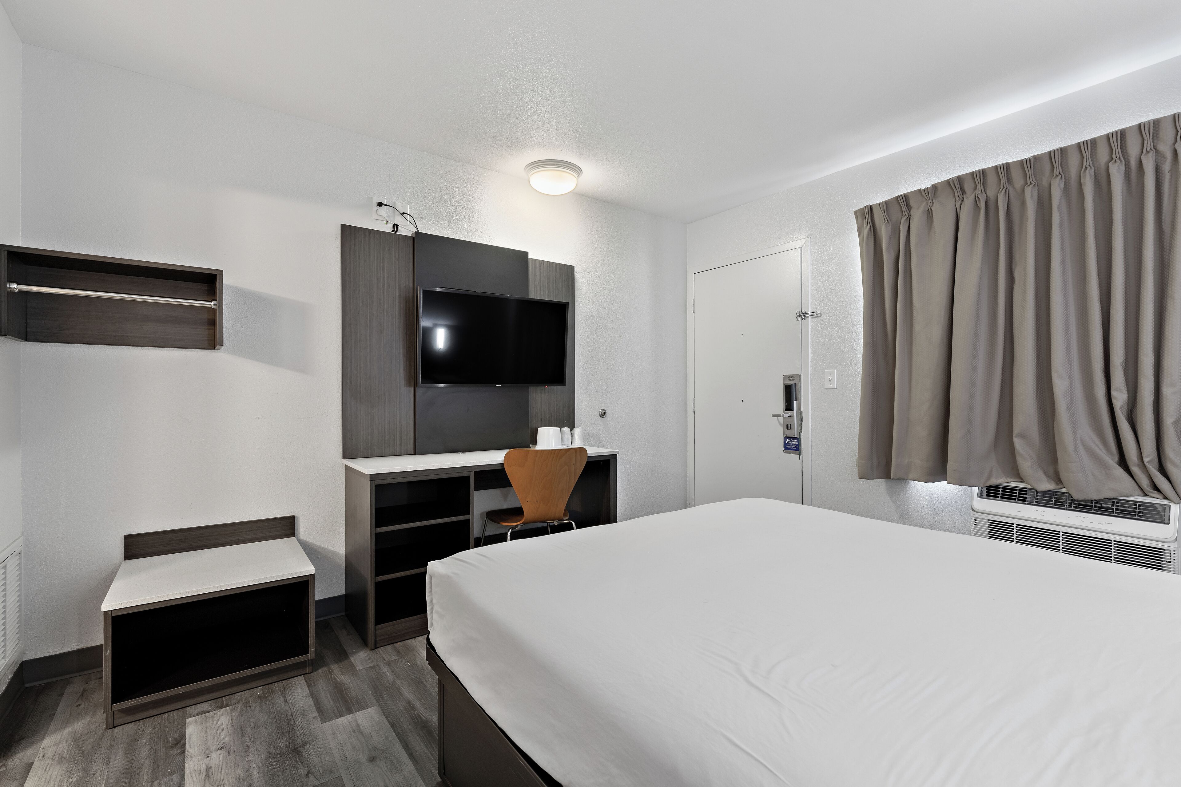 A hotel room with a bed, a desk with a chair, a television, and a wardrobe.