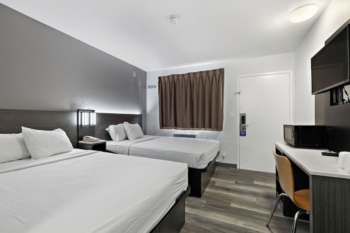 Una habitación de hotel con dos camas, un escritorio, una silla, un televisor y la puerta del baño.