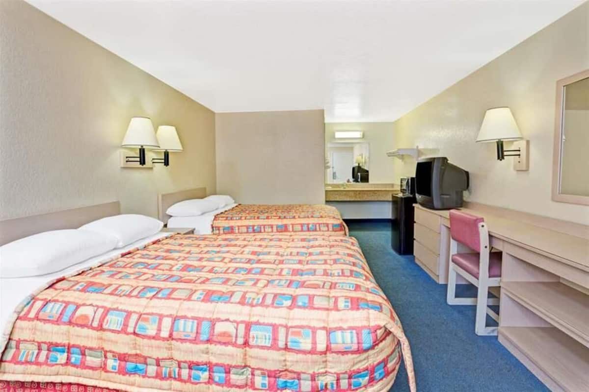 Ein Hotelzimmer mit zwei Betten, einem Schreibtisch, einem Sessel, einem Fernseher und einem Spiegel.