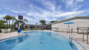 A swimming pool with a sign for Knights Inn, surrounded by palm trees and outdoor seating.