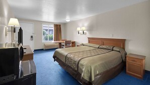 A hotel room with a large bed, a desk with a lamp, a chair, a nightstand, and a television.
