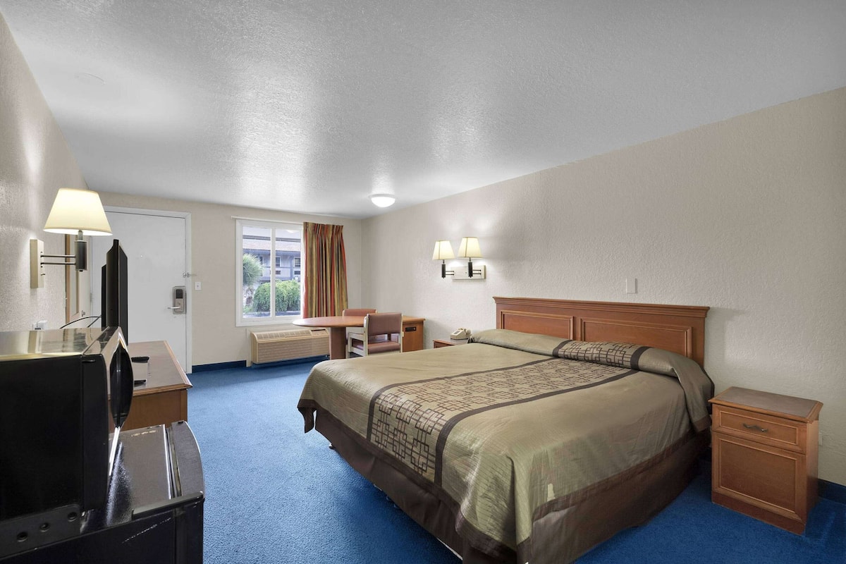 Ein Hotelzimmer mit einem großen Bett, einem Schreibtisch mit Lampe, einem Sessel, einem Nachttisch und einem Fernseher.