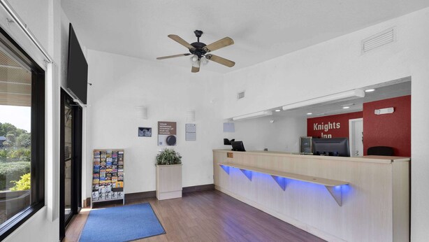 A reception area with a wooden reception desk, a ceiling fan, a blue mat, and a sign for Knights Inn.