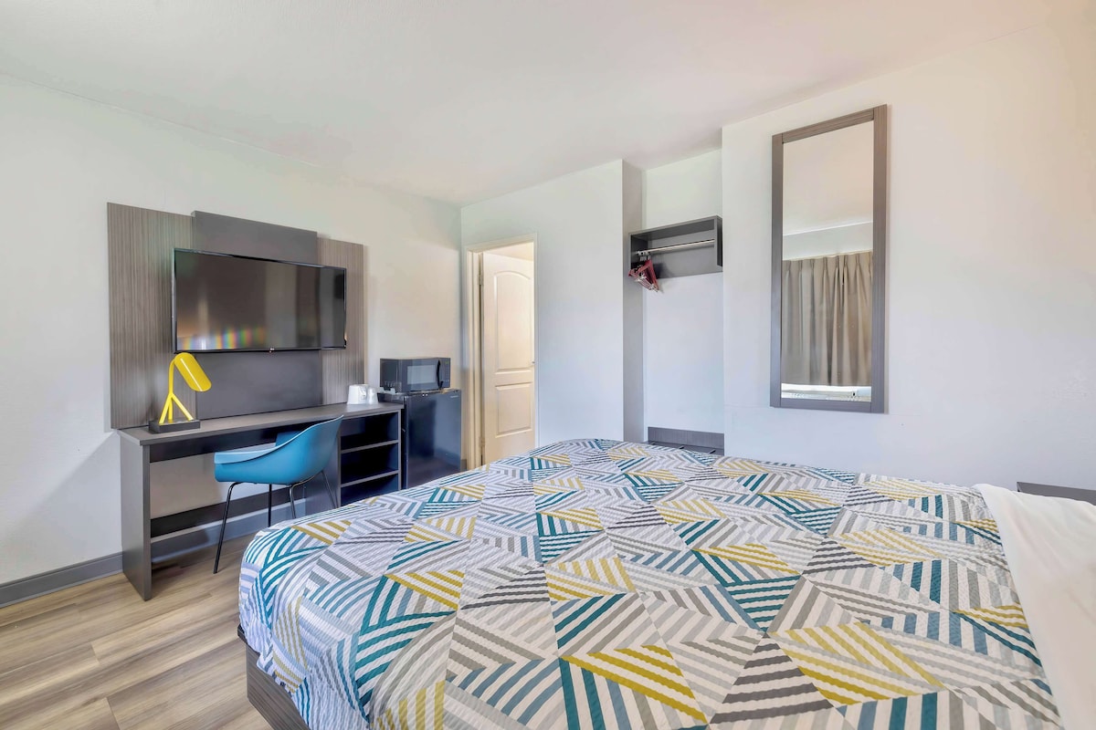 A hotel room with a bed, a desk, a chair, a TV, and a mirror.
