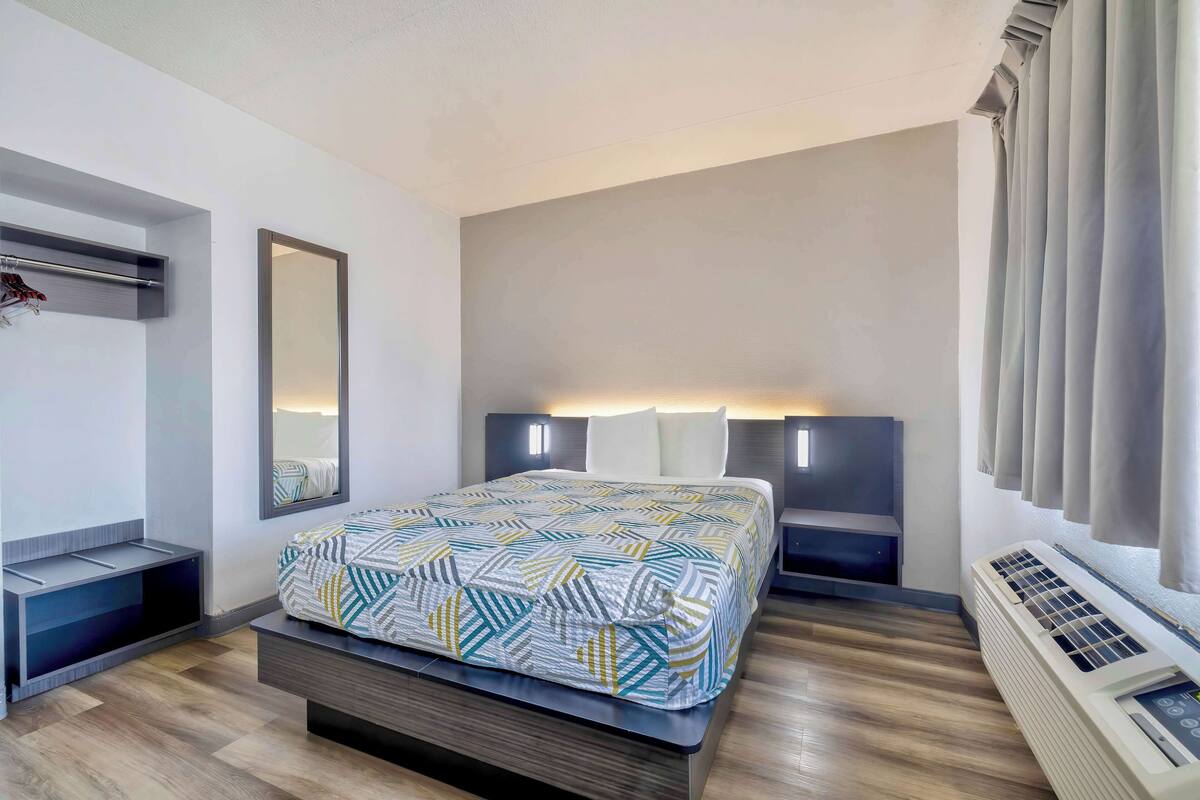 A modern bedroom with a bed, bedside tables, a mirror, and a wall-mounted air conditioner.